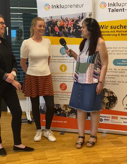 Drei Personen in einer Interviewsituation. Amy Zayed hält Mikrophon.
